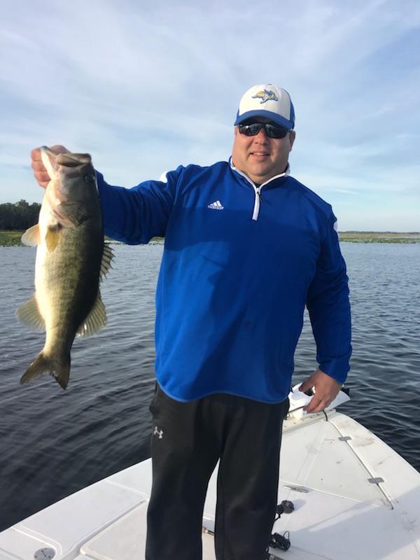 Fisherman in blue holding a bass on the boat