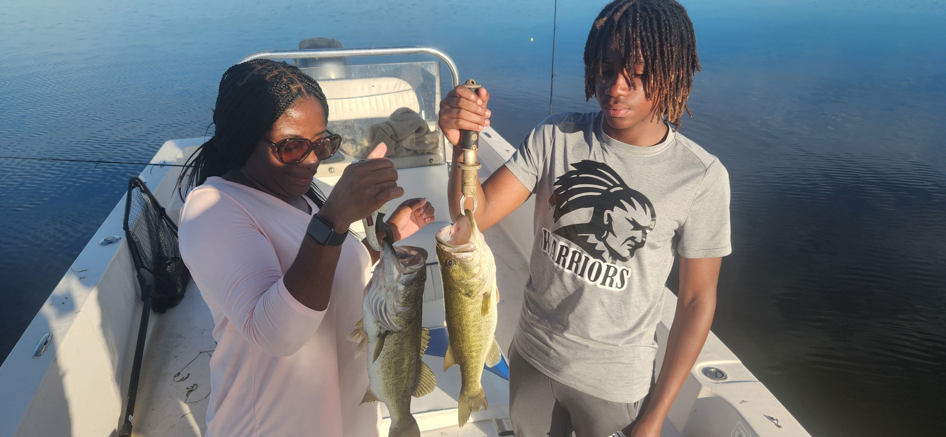 Two young anglers showing their bass catch on the water